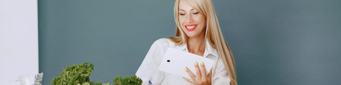 Woman using a tablet surrounded by fresh vegetables at a table, showcasing healthy lifestyle and technology.