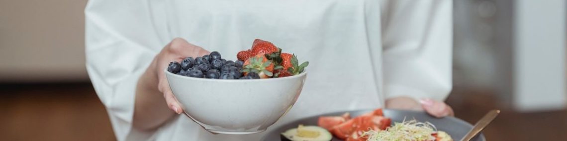 Person holding a bowl of fresh berries and a plate with avocado toast, displaying a healthy breakfast spread.