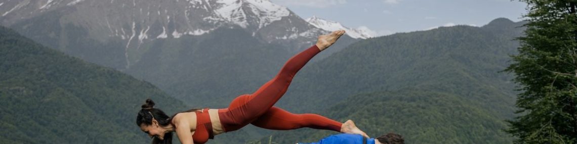 Couple doing yoga exercises outdoors with a breathtaking mountain view.
